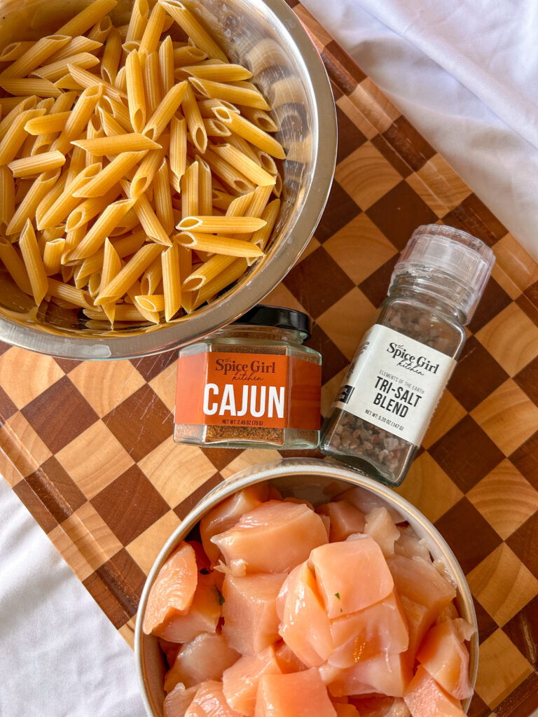 Ingredients for creamy Cajun chicken pasta including chicken, penne pasta, olive oil, and Cajun seasoning