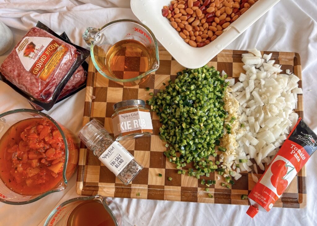 Ingredients for spicy bison chili including ground bison, fresh peppers, beans, fire-roasted tomatoes, Modelo, and Okie Rub