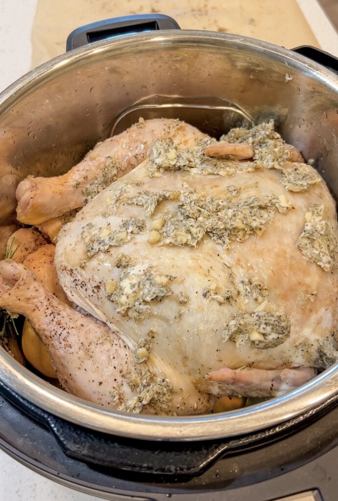 Whole chicken on the Instant Pot trivet with chicken broth, lemon, and fresh rosemary ready to cook