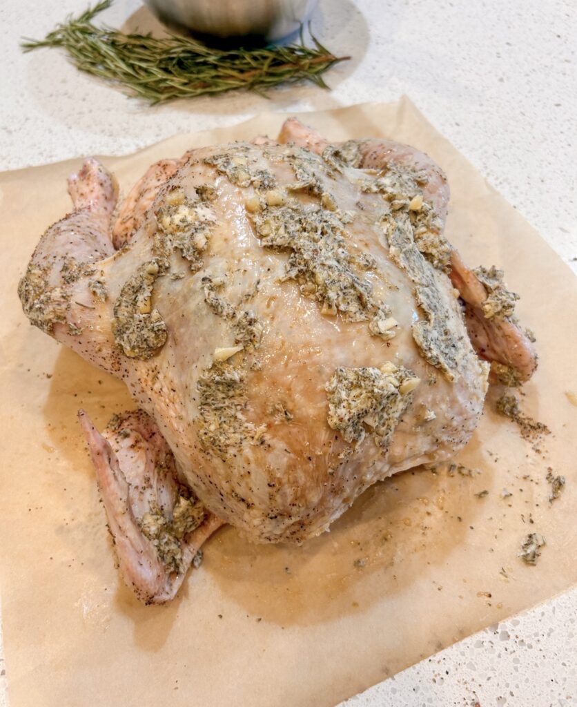Spreading honey herb butter underneath the skin of a whole chicken before cooking