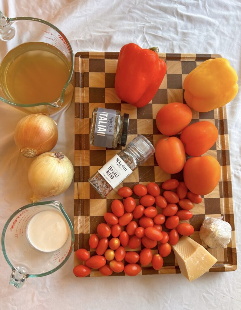 Fresh ingredients for roasted red pepper and tomato soup including Roma tomatoes, cherry tomatoes, bell peppers, onion, and garlic
