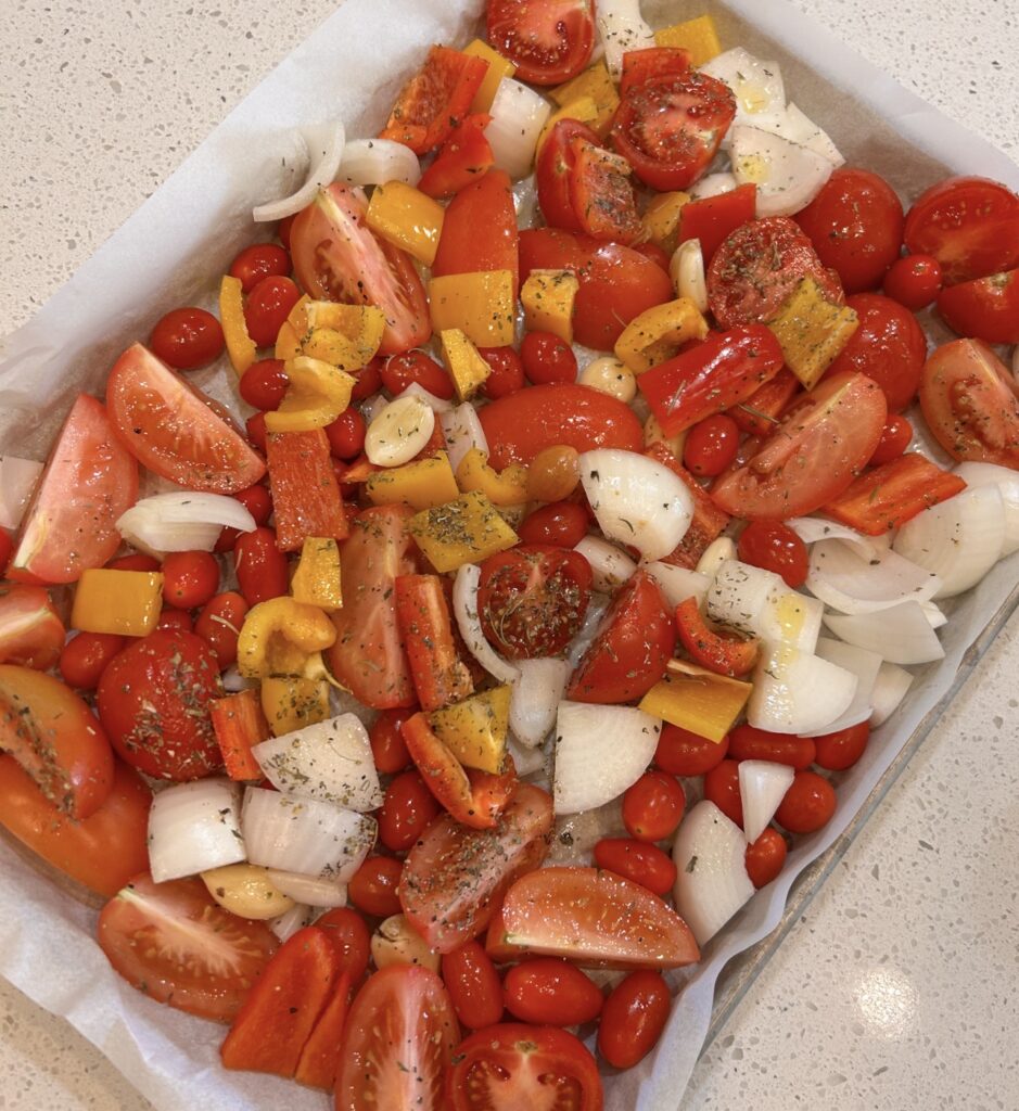 Fresh tomatoes, bell peppers, onion, and garlic seasoned on a sheet pan before roasting