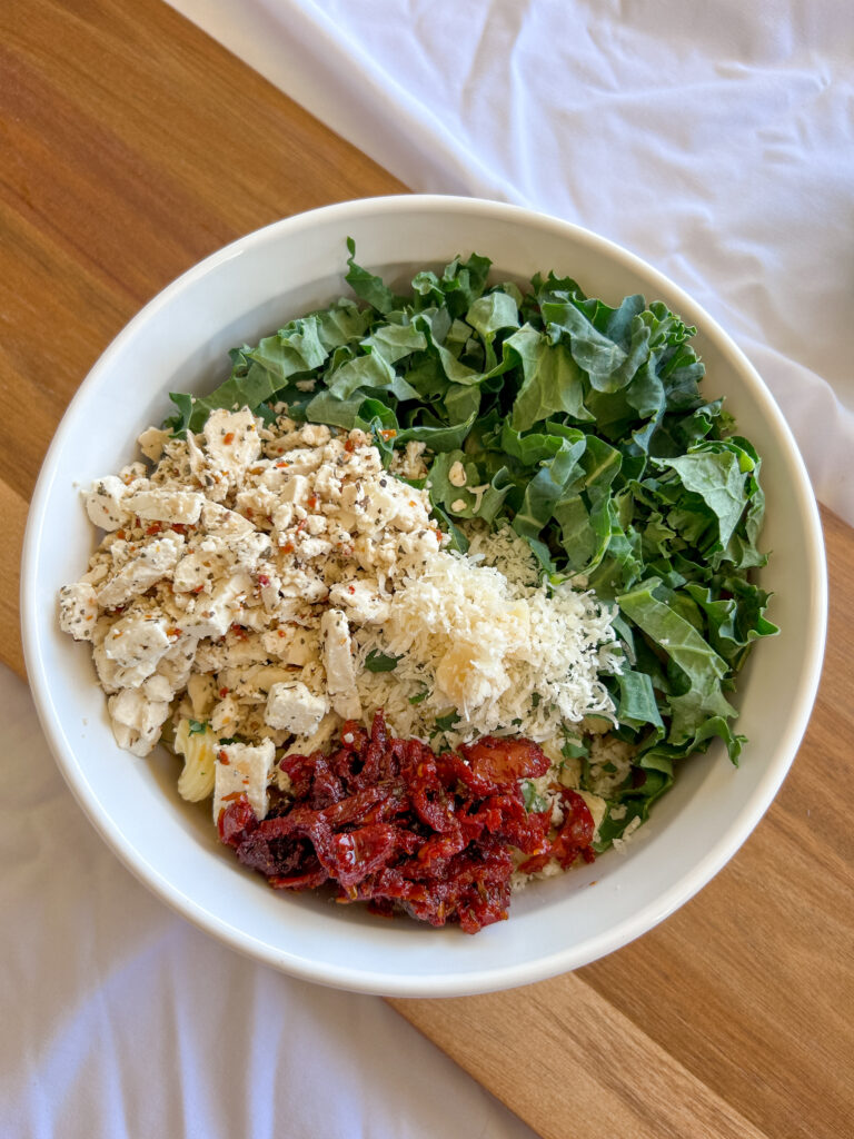 Tossing pasta, kale, feta, and sun-dried tomatoes with basil vinaigrette