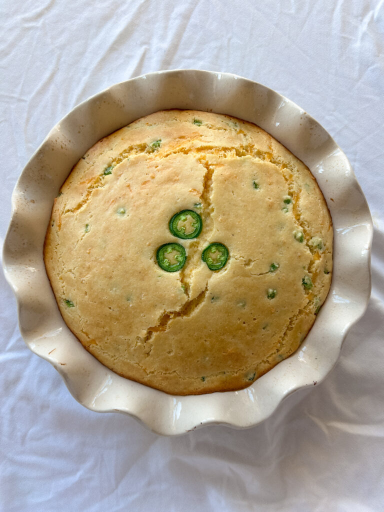 Freshly baked jalapeño cheddar cornbread in an 8-inch pie pan, golden on top with melted cheddar and diced jalapeños visible.