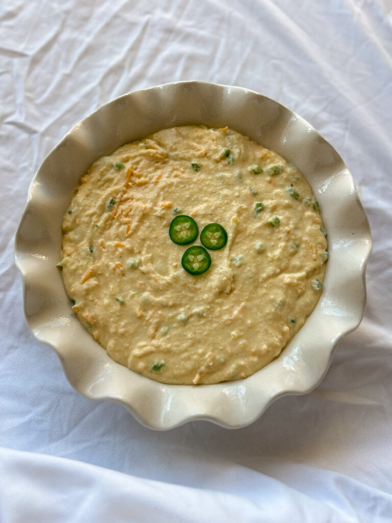 Pouring jalapeño cheddar cornbread batter into pie pan