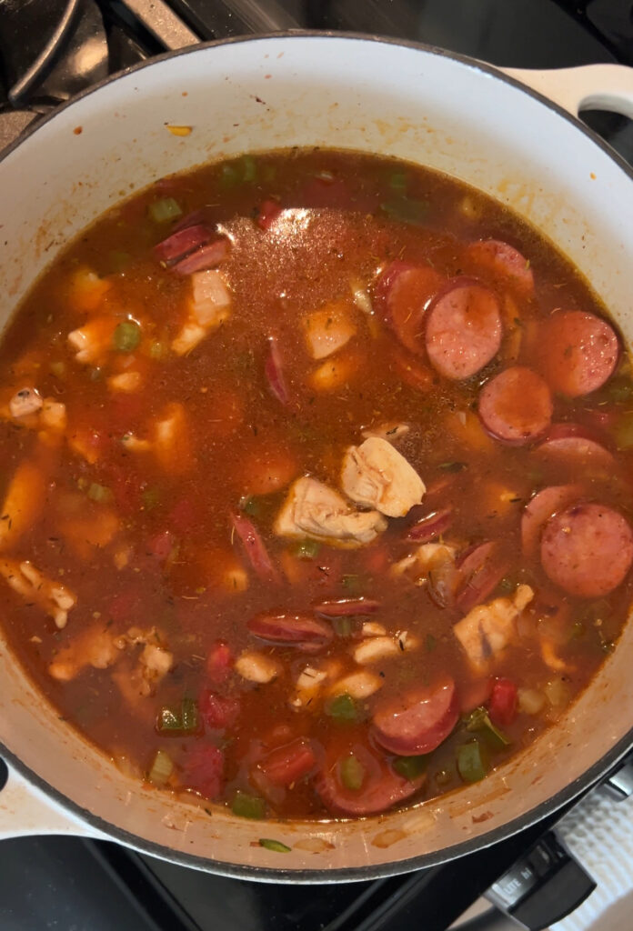 adding diced tomatoes broth sausage and chicken to dutch oven for pastalaya