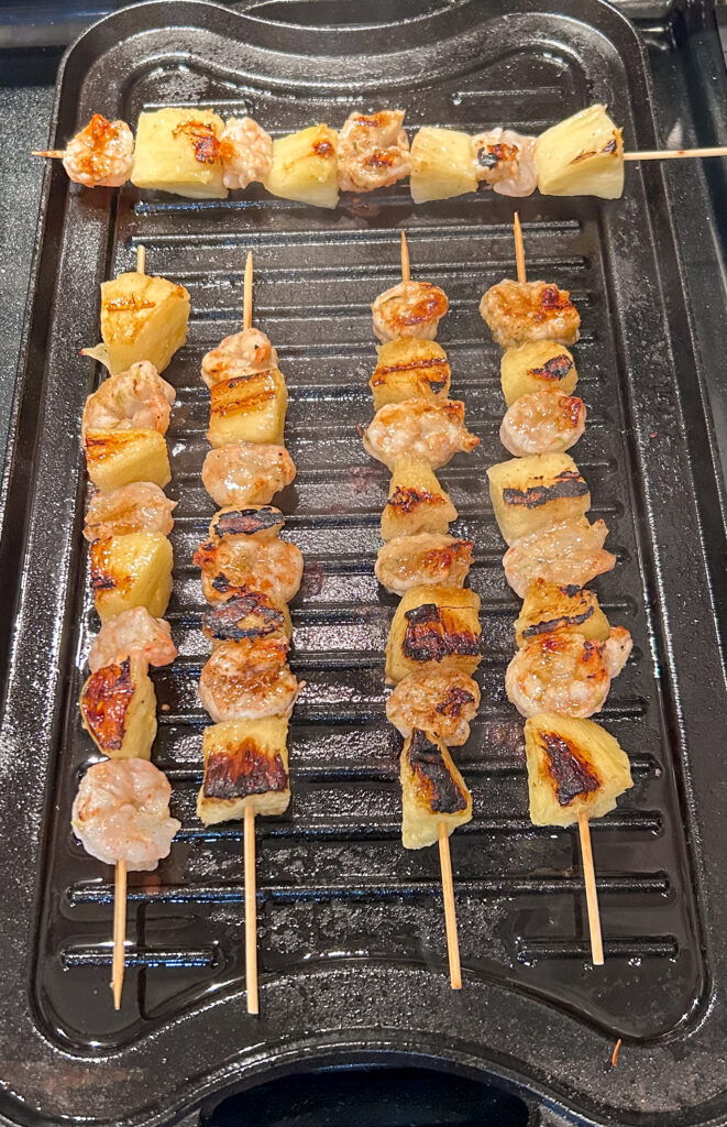 shrimp and pineapple skewers cooking on a cast iron grill pan
