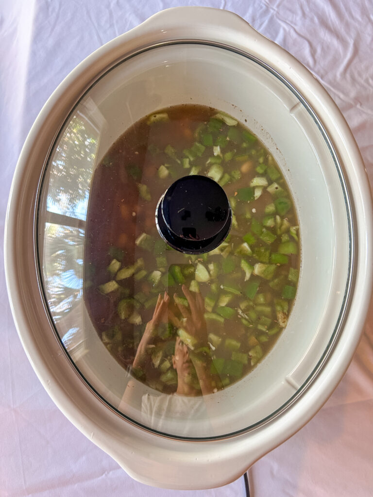 Slow cooker filled with green chile chicken stew ingredients with the lid on before cooking