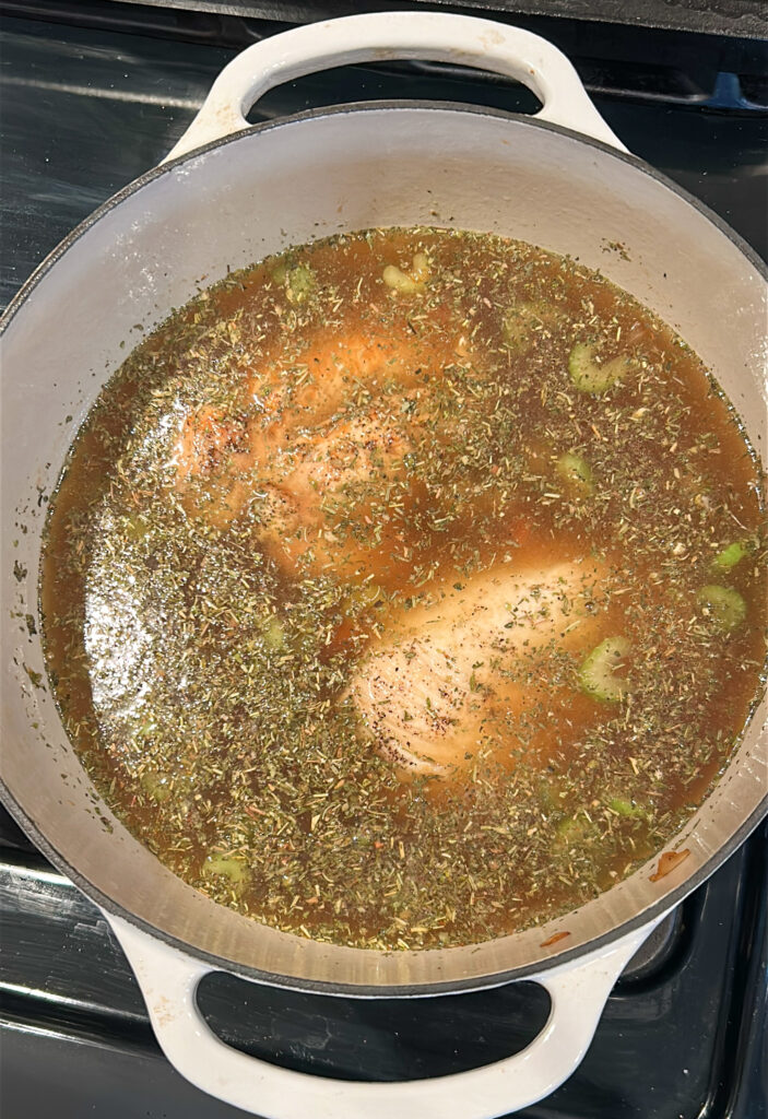 Adding broth and chicken to chicken soup on stove