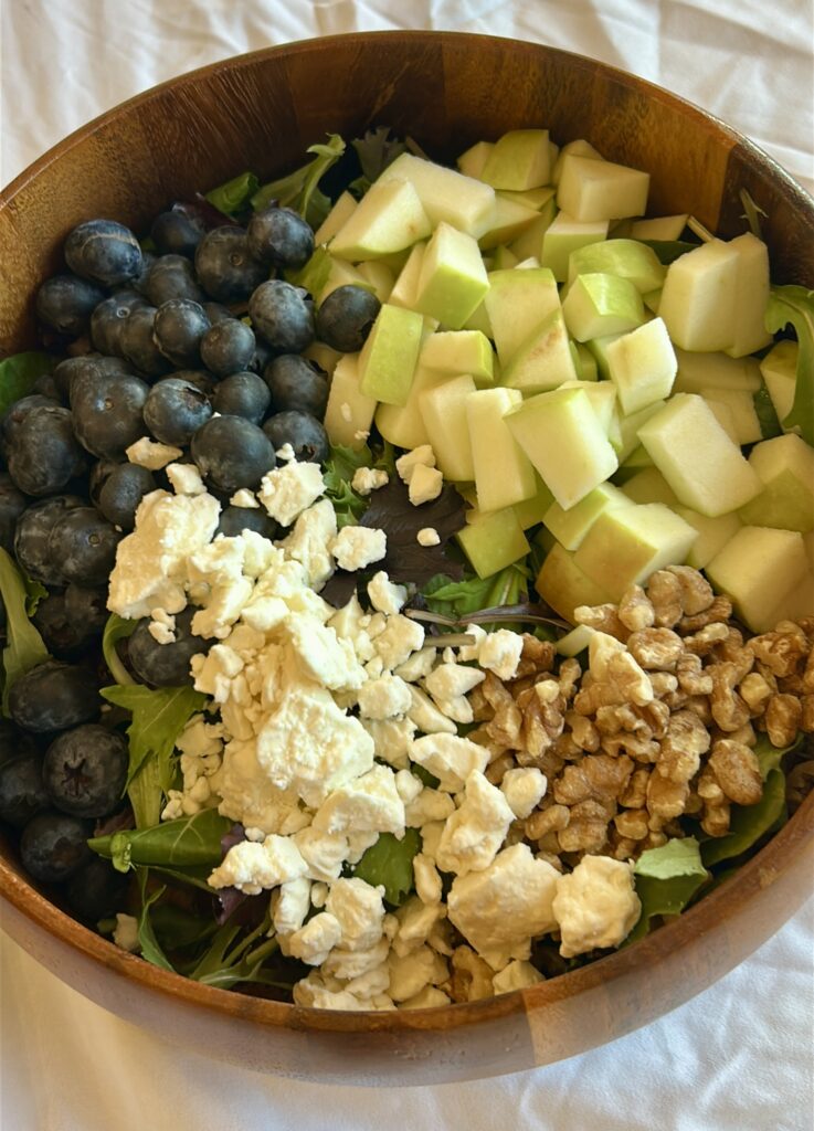 adding blueberries apples feta and walnuts to mixed greens for blueberry apple salad