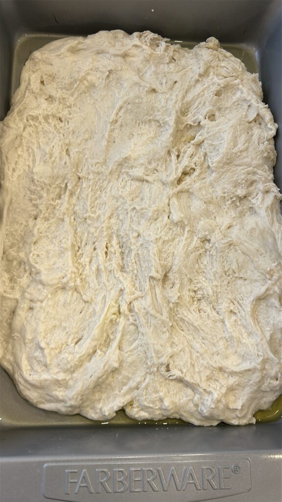 Greek focaccia dough after second rise in oiled baking pan