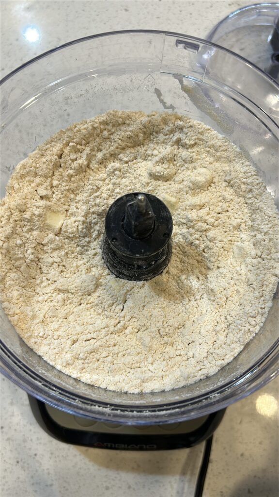Pulsing flour, turmeric, and butter in food processor for flaky Jamaican meat pie dough