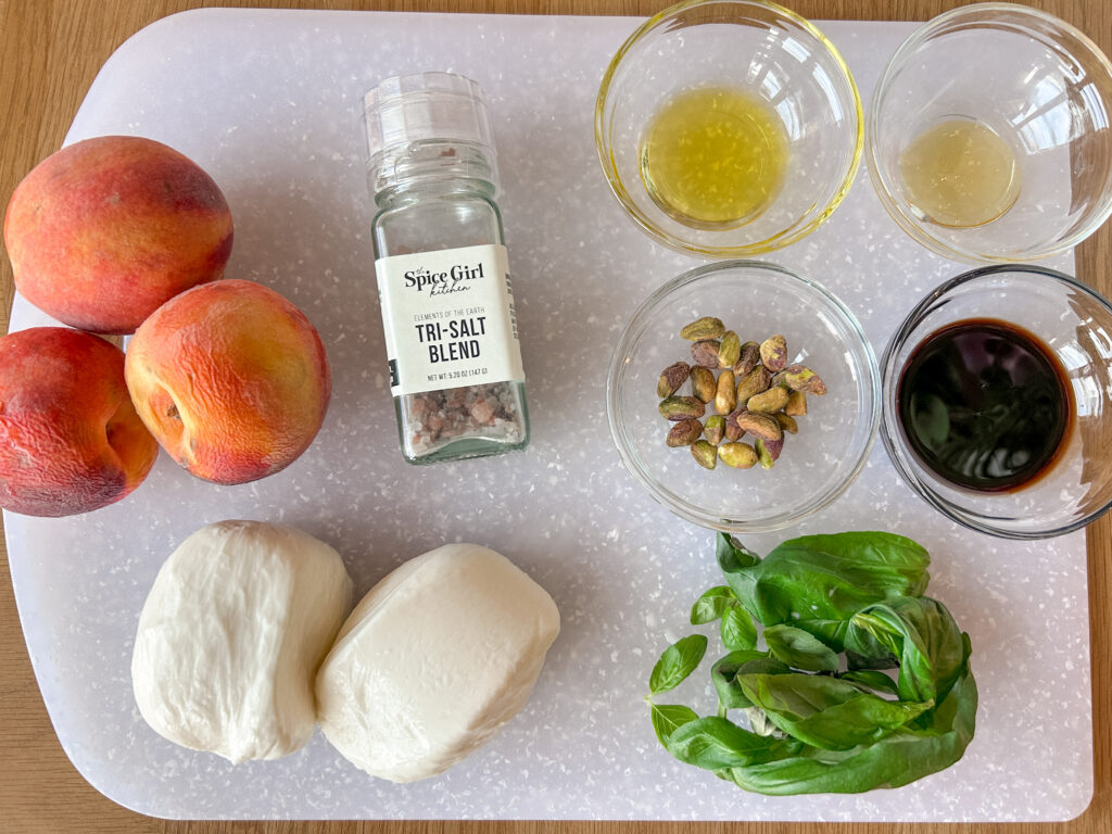 Ingredients for peach caprese salad including peaches, burrata, basil, and balsamic glaze