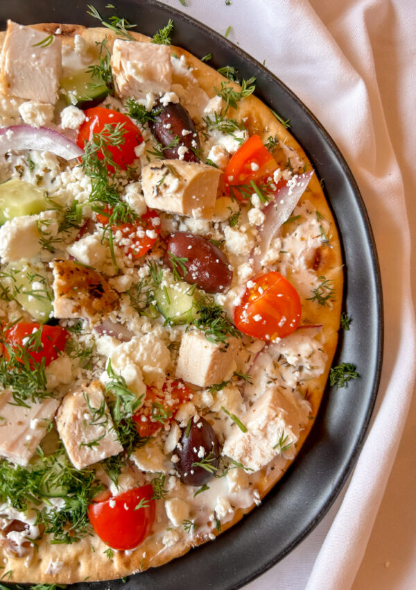 close up of mediterranean flatbread showing yogurt sauce, feta, and fresh toppings