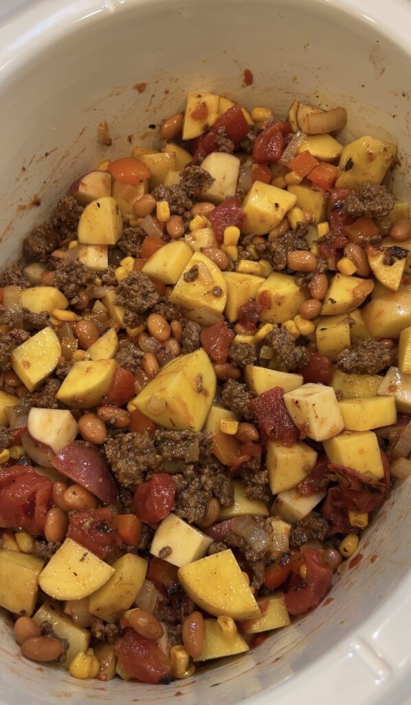 Ground beef, potatoes, beans, corn, tomatoes, and broth added to the slow cooker for cowboy casserole