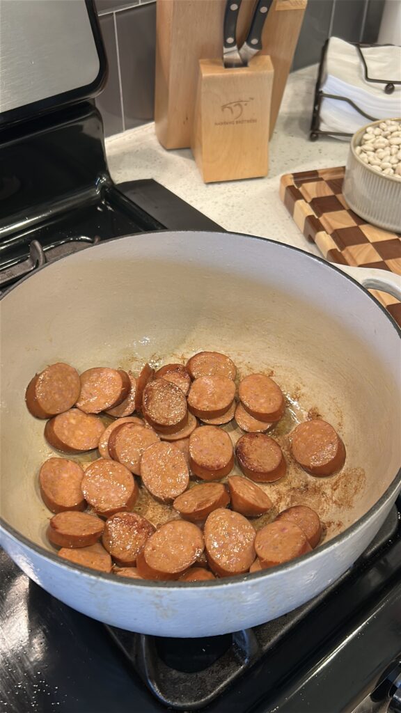 Andouille sausage browning in a Dutch oven for white beans and sausage