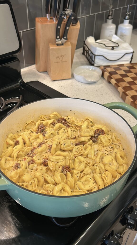 Heavy cream, Parmesan cheese, and sun-dried tomatoes being stirred into Marry Me Tortellini