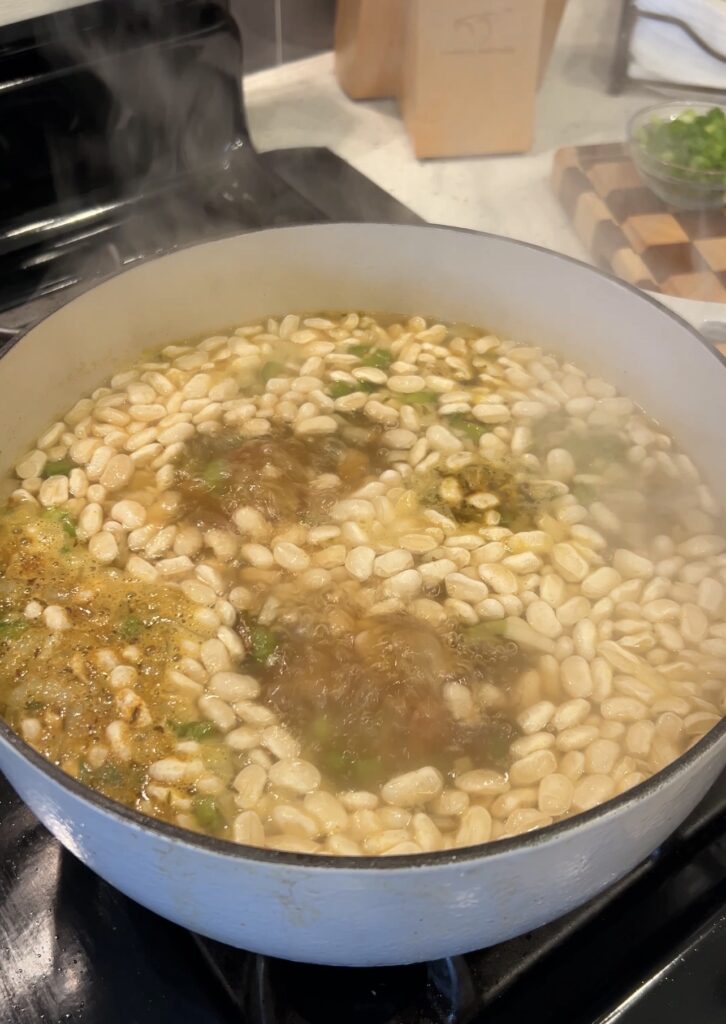 White beans and sausage simmering in a pot with Cajun seasoning and bay leaf