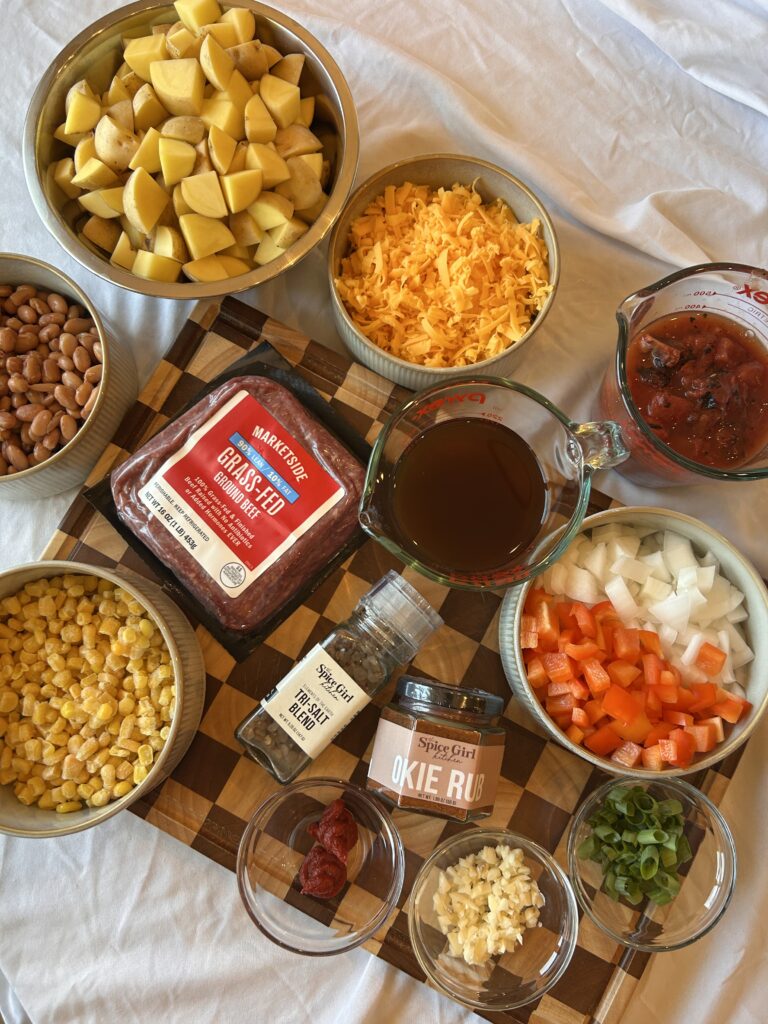 Ingredients needed to make slow cooker cowboy casserole including ground beef, potatoes, pinto beans, corn, cheddar cheese, and Okie Rub