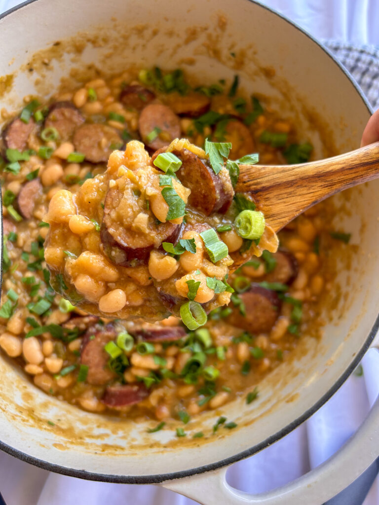 Close up of creamy white beans and andouille sausage garnished with green onions and parsley