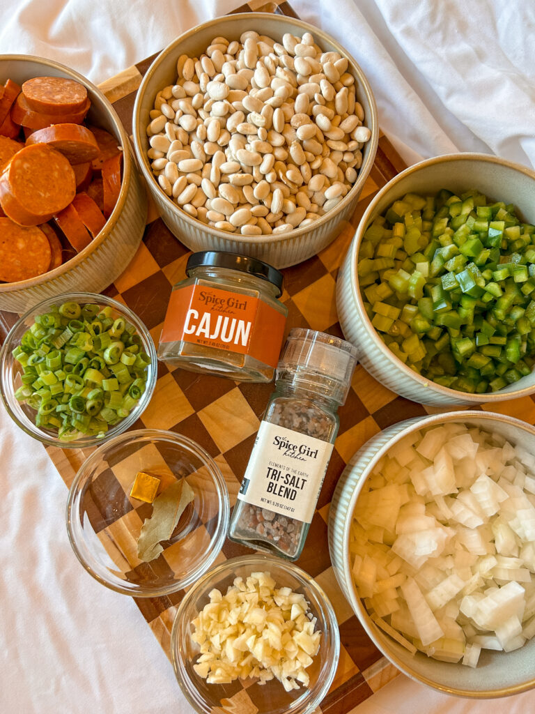 Ingredients for white beans and sausage including dried white beans, andouille sausage, onion, celery, bell pepper, and Cajun seasoning