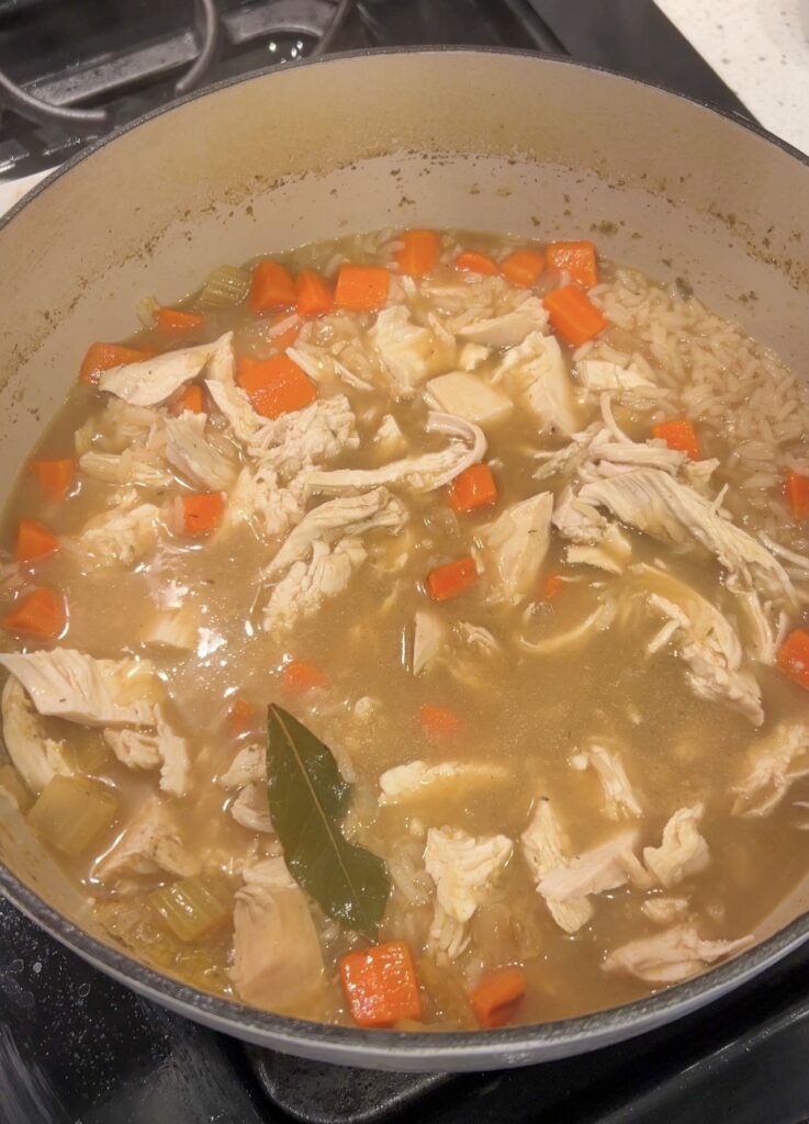 Rice cooking in broth with shredded chicken added back to Greek lemon chicken soup