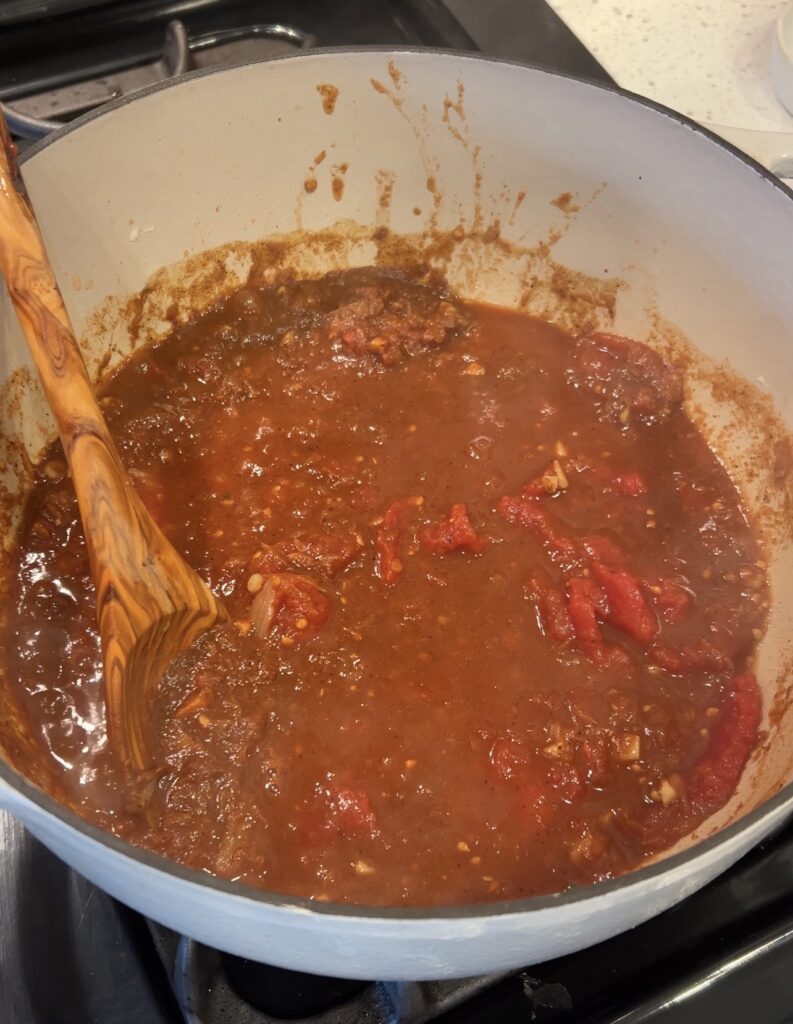 Crushed whole peeled tomatoes being added to Moroccan white bean stew