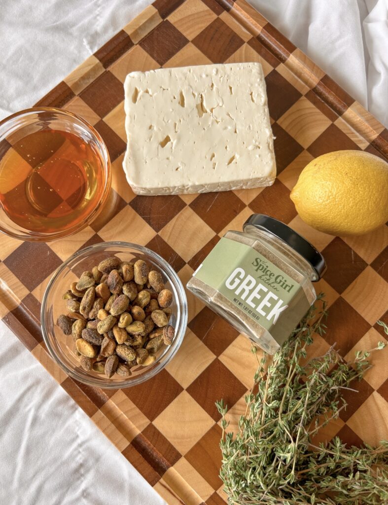 Ingredients for baked feta including feta cheese, honey, pistachios, olive oil, Greek seasoning, lemon, and fresh thyme.