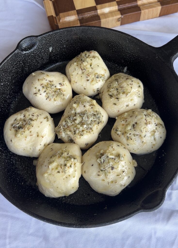 Unbaked pizza bombs brushed with Italian garlic butter before baking in a cast iron skillet.