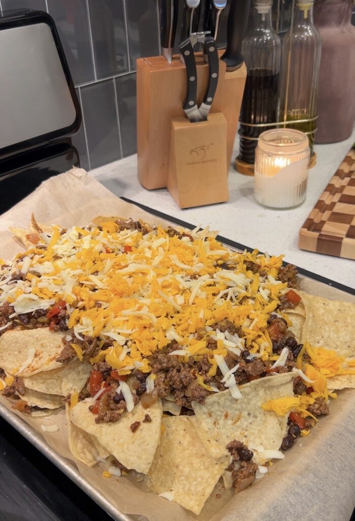 Layering tortilla chips with seasoned beef and shredded cheese for sheet pan nachos