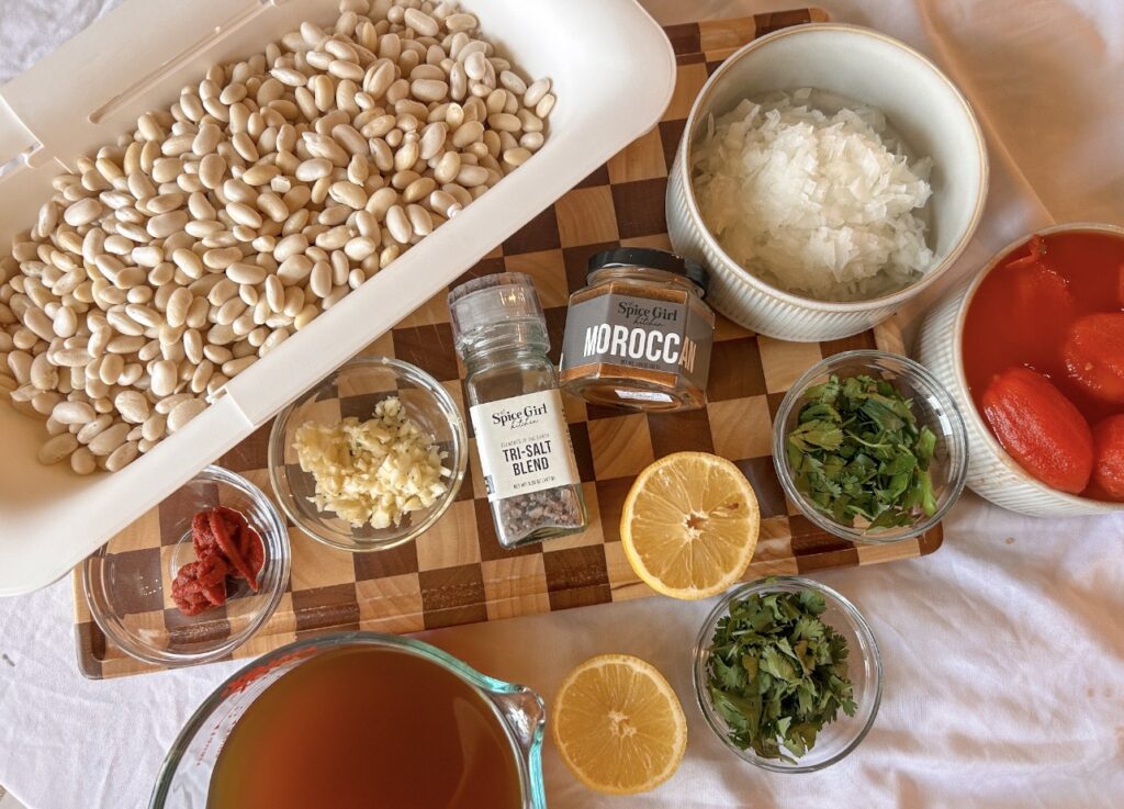 Ingredients needed to make authentic Loubia including cannellini beans, tomatoes, onion, garlic, fresh herbs, and Moroccan seasoning