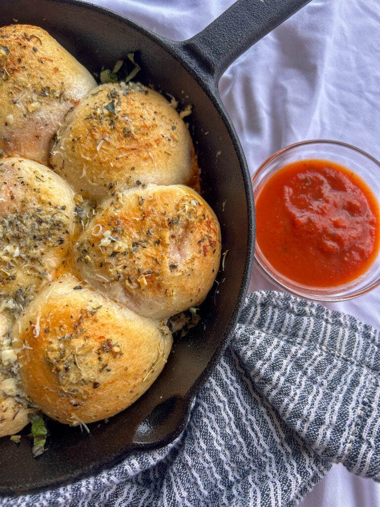 Golden brown pizza bombs baked in a cast iron skillet with melted mozzarella, pepperoni, Italian garlic butter, Parmesan, and marinara dipping sauce.