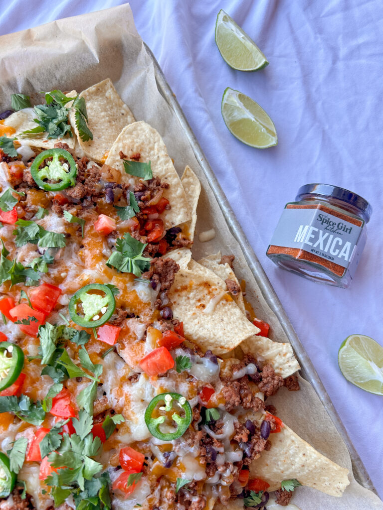 Sheet pan nachos recipe topped with seasoned ground beef, black beans, melted cheese, avocado, tomatoes, cilantro, and jalapeños