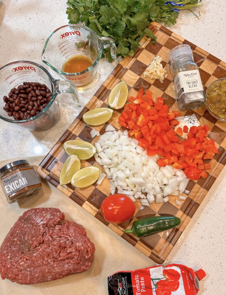 Ingredients needed to make sheet pan nachos including tortilla chips, ground beef, black beans, cheese, vegetables, and toppings