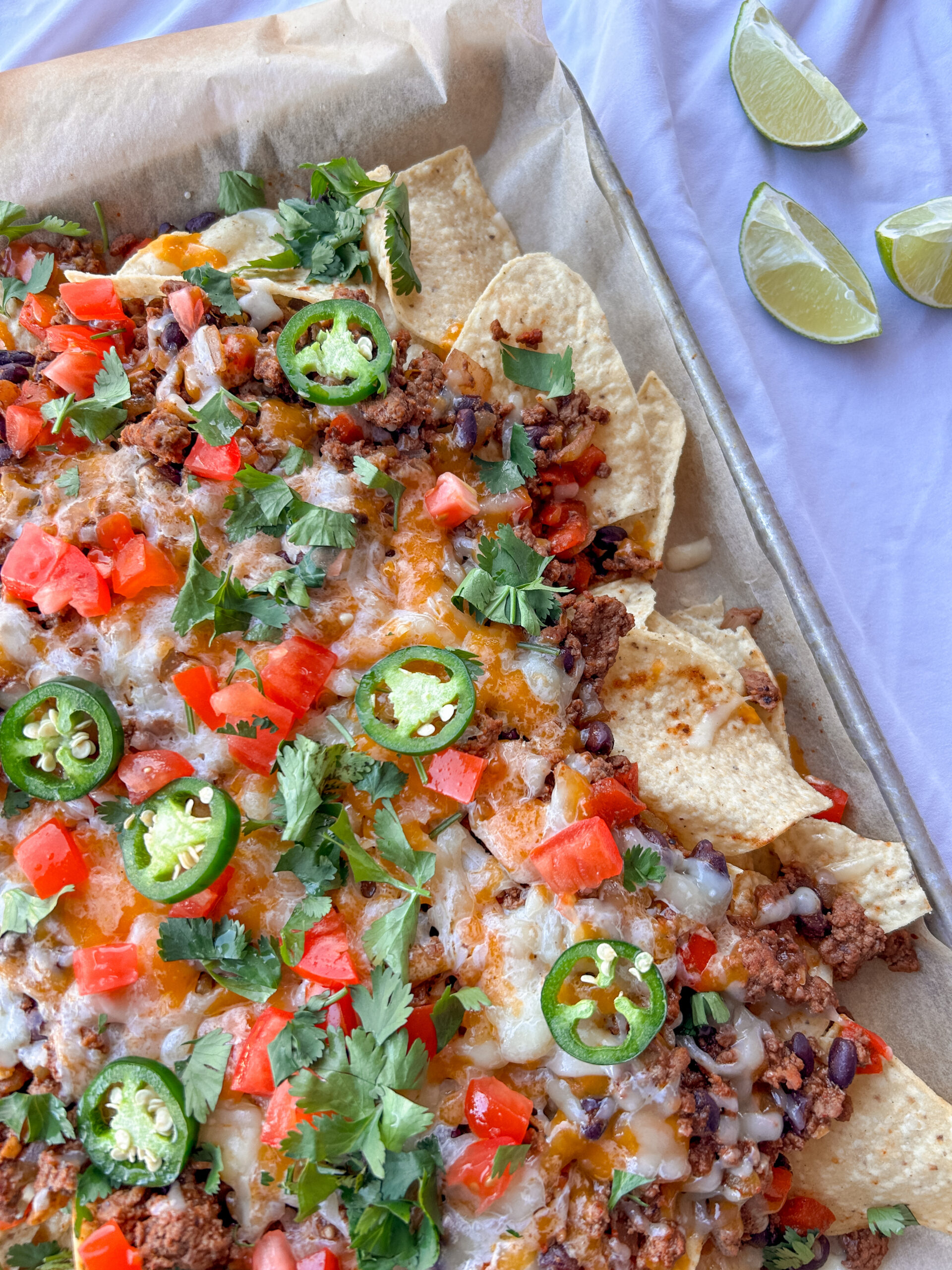 Sheet pan nachos recipe topped with seasoned ground beef, black beans, melted cheese, avocado, tomatoes, cilantro, and jalapeños