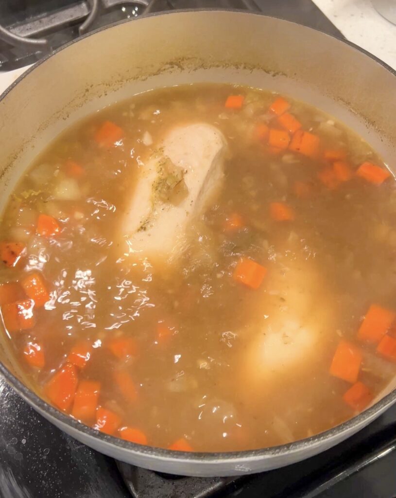Chicken simmering in broth with vegetables for Greek lemon chicken soup