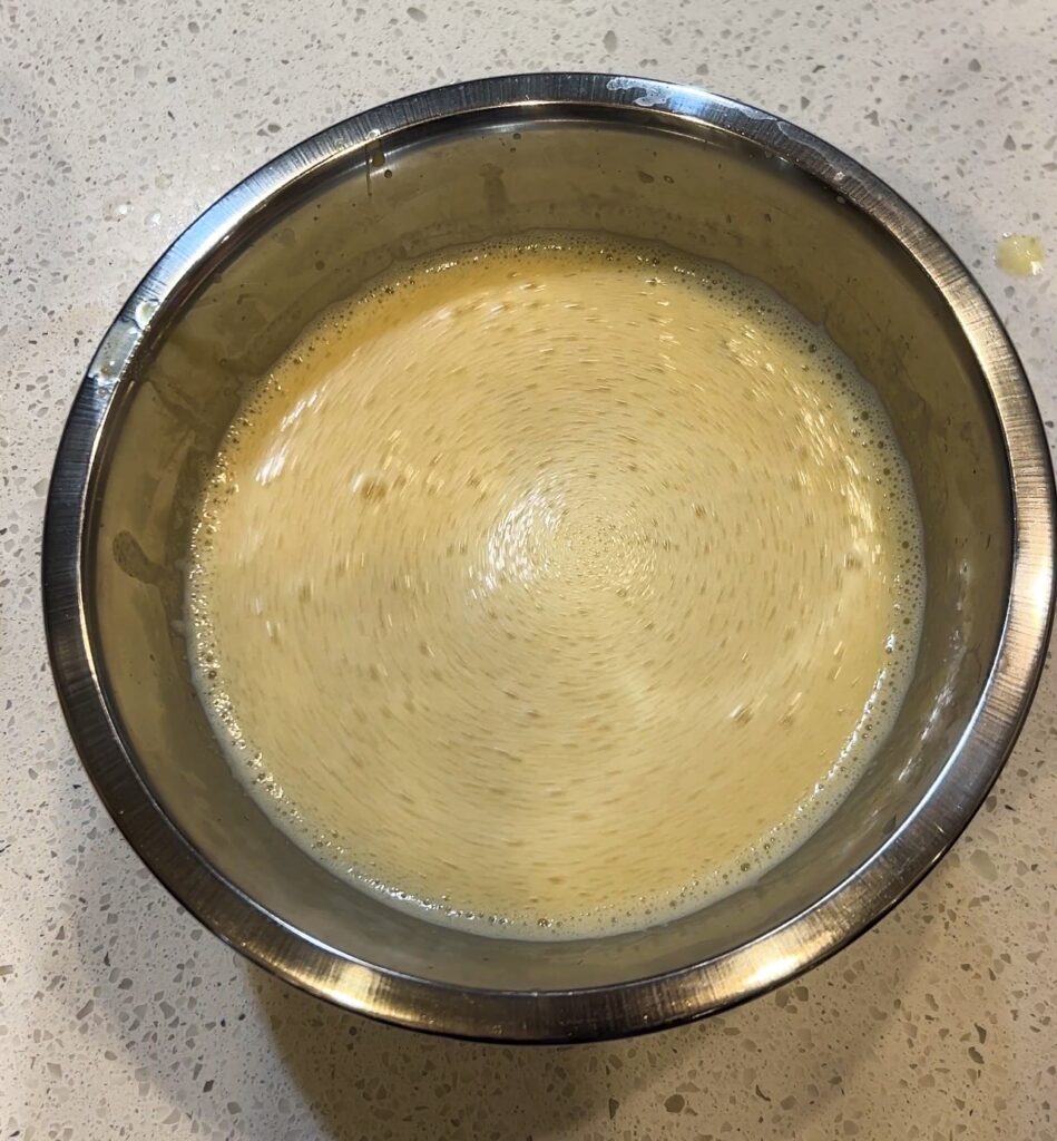 Hot broth being whisked into the lemon and egg mixture to temper it for Greek lemon chicken soup