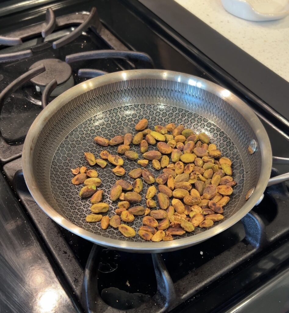 Toasting pistachios in a skillet for baked feta with honey.
