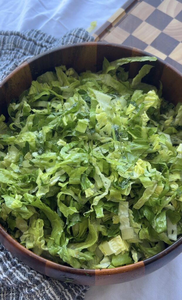 Tossing maroulosalata with lemon olive oil dressing until evenly coated