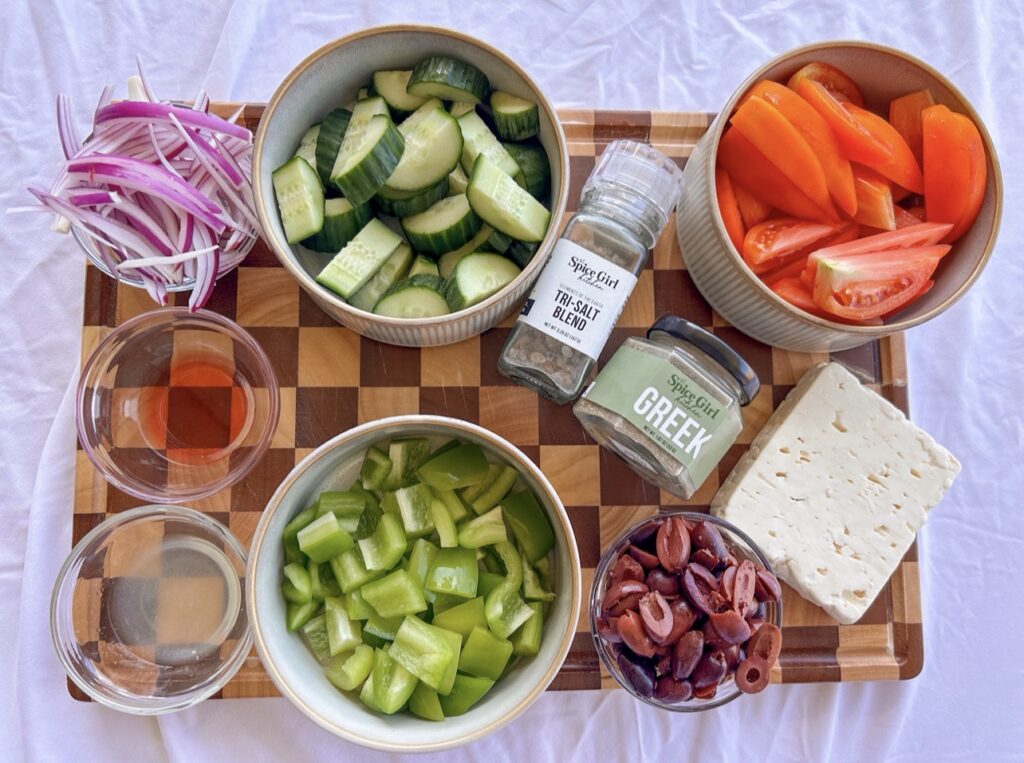 Ingredients for Traditional Greek Salad including tomatoes, cucumber, green bell pepper, red onion, Kalamata olives, feta, olive oil, and Greek Seasoning