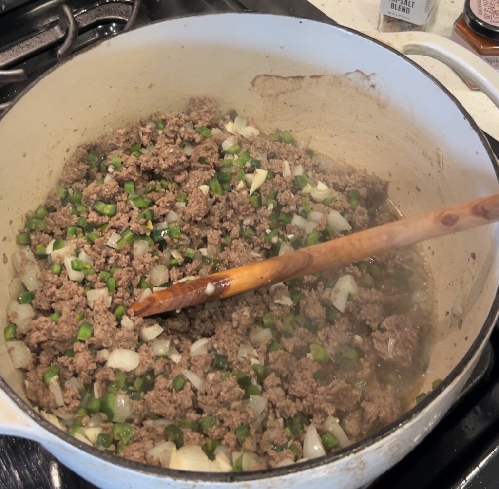 Fresh poblano peppers, jalapeños, and onion cooking with ground bison for spicy bison chili
