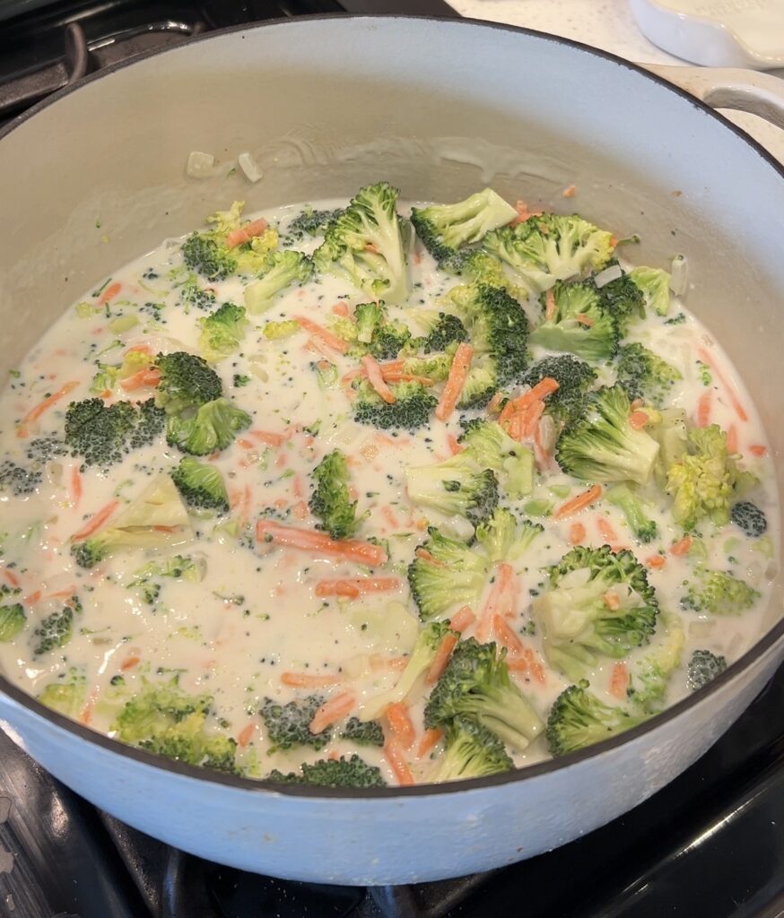 Chopped broccoli and carrots simmering in creamy broccoli cheddar soup