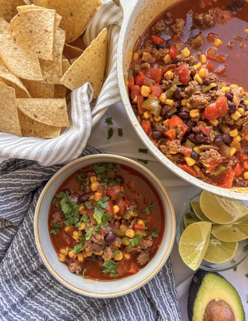 Ground beef taco soup with black beans, corn, tomatoes, fresh peppers, and taco toppings