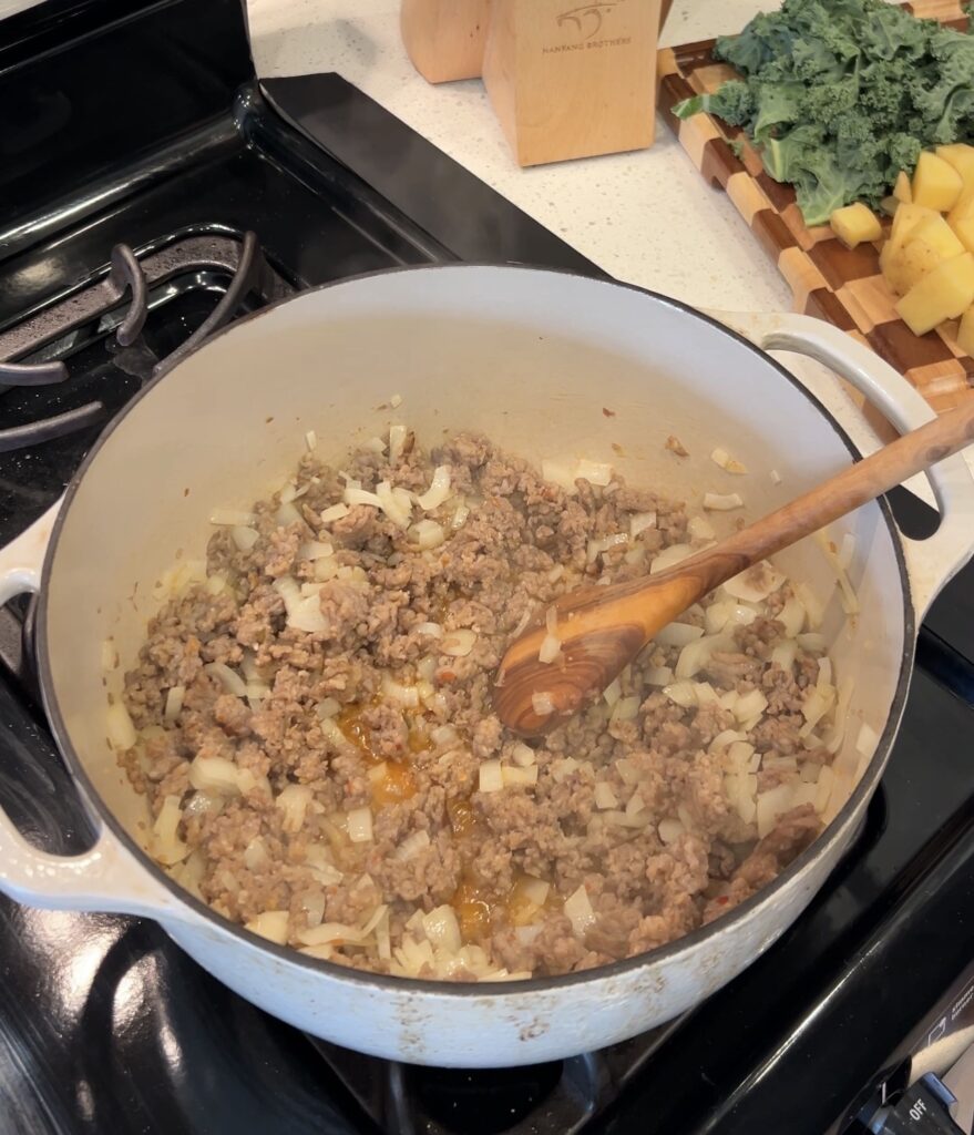 Onion and garlic sautéing with browned Italian sausage for Zuppa Toscana