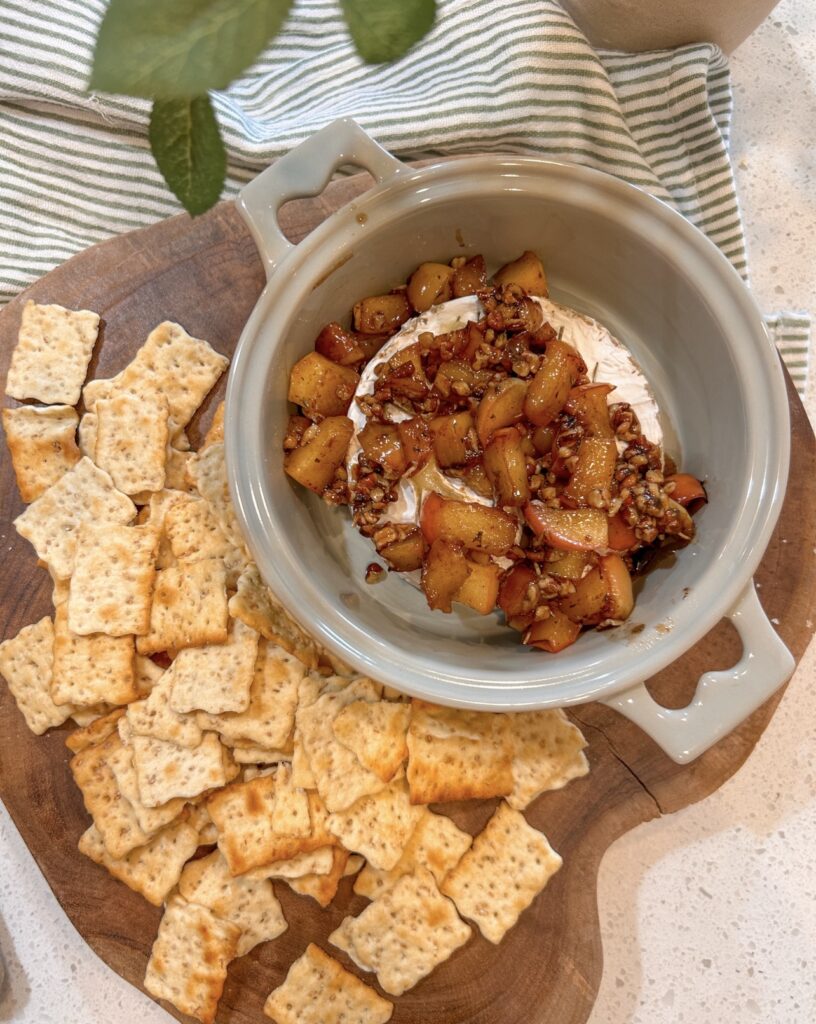 Maple apple and pecan topping being spooned over baked Brie