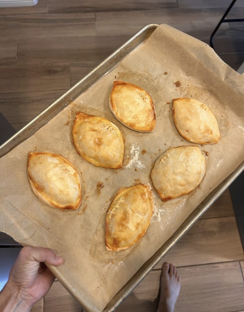 Golden brown football-shaped buffalo chicken hand pies with decorative pastry laces after baking.