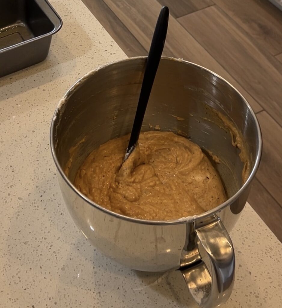 Thick orange pumpkin bread batter being mixed until smooth and combined.