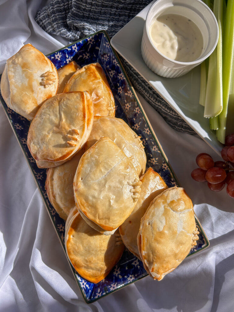 Buffalo chicken hand pies shaped like footballs with golden flaky crusts and pastry laces.