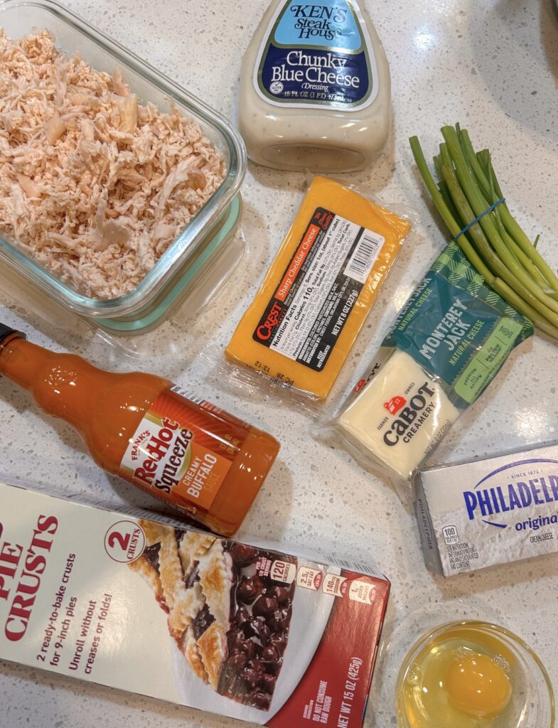 Ingredients for buffalo chicken hand pies including shredded chicken, buffalo sauce, cream cheese, shredded cheese, and pie crust.