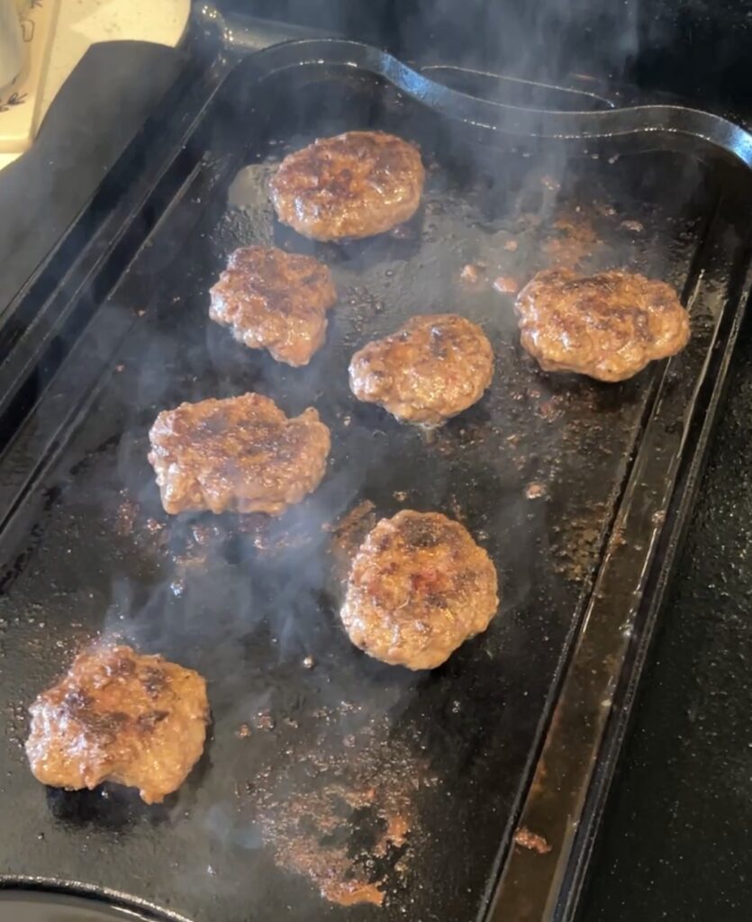 Small Okie Rub-seasoned burger patties cooking in a skillet